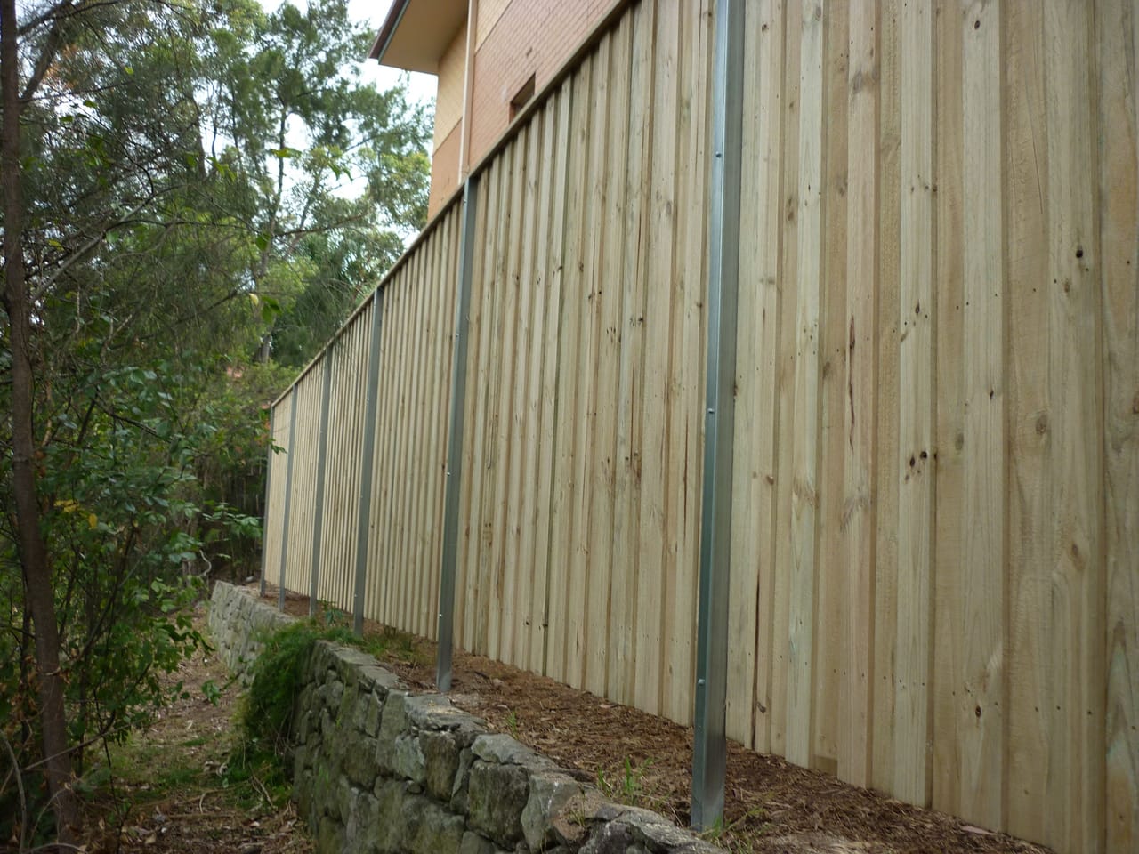 Lap and cap treated pine timber fence with a timber capping rail along the top, built above an existing sandstone retaining wall in Sydney