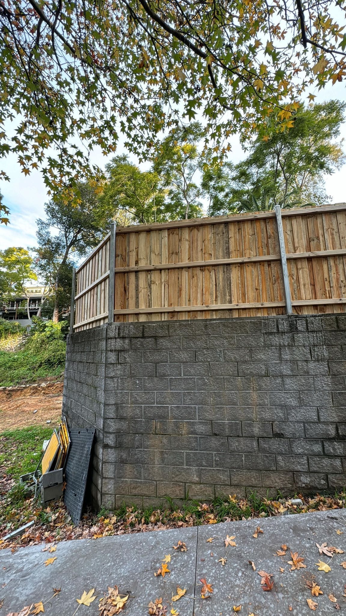 Treated pine timber fence above a block wall boundary with fallen leaves on the driveway below