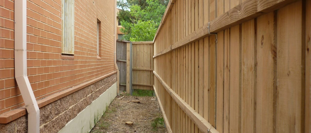 Tall treated pine timber fence installed along a narrow side boundary between a brick house and the neighbouring property